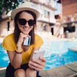 Woman sitting at the swimming pool and using credit card to make an online hotel reservation